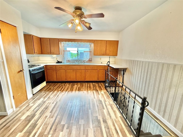 kitchen featuring light wood-style floors, light countertops, brown cabinetry, and gas range