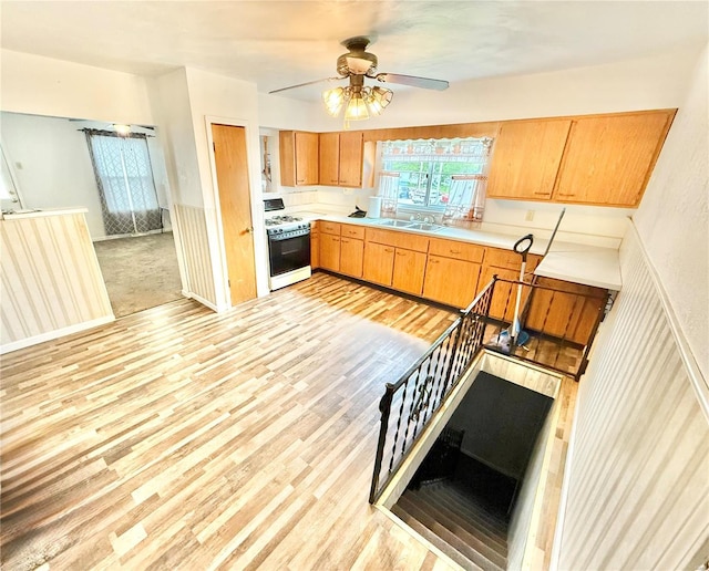 kitchen with a ceiling fan, white gas range oven, light countertops, a sink, and light wood-style flooring