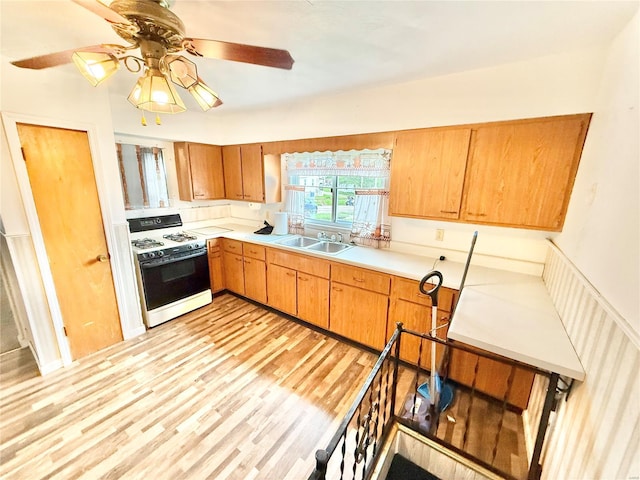 kitchen with a ceiling fan, white gas stove, light wood-type flooring, light countertops, and a sink