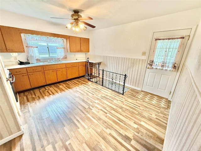 kitchen featuring light countertops, light wood-style flooring, a ceiling fan, and wainscoting
