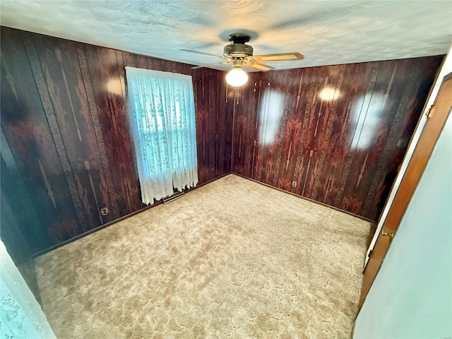 carpeted empty room with wood walls and ceiling fan