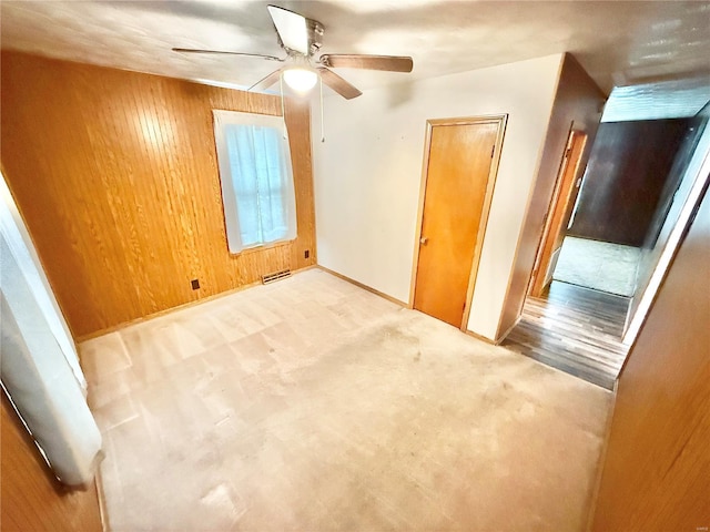 carpeted spare room with visible vents, baseboards, ceiling fan, and wooden walls