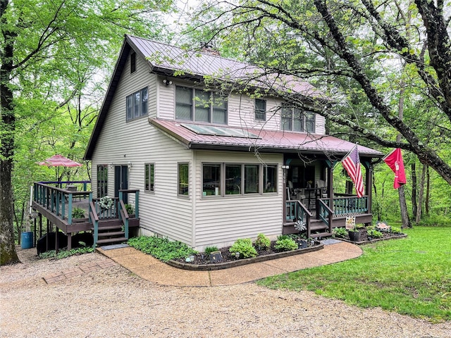 view of front of property with a wooden deck, covered porch, a front lawn, and metal roof