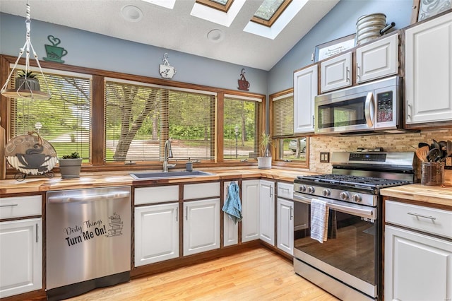 kitchen with a sink, wood counters, white cabinetry, lofted ceiling with skylight, and appliances with stainless steel finishes