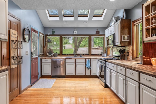 kitchen with light wood finished floors, a sink, butcher block countertops, backsplash, and appliances with stainless steel finishes