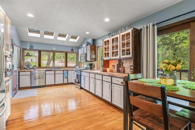 kitchen featuring a textured ceiling, glass insert cabinets, a sink, light wood-style floors, and stainless steel appliances
