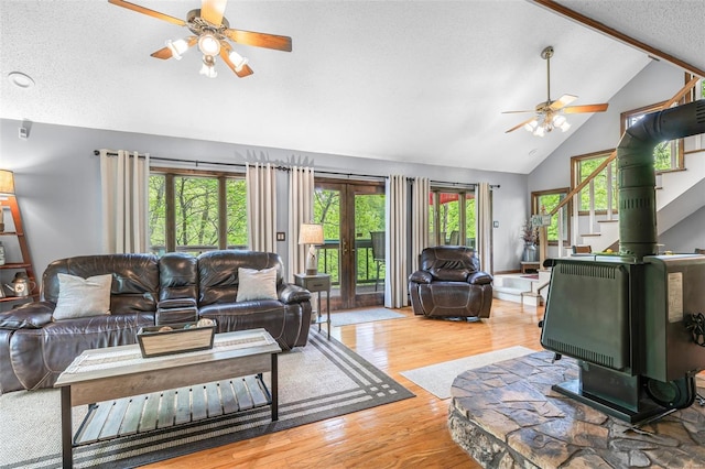living area with wood finished floors, a wood stove, a textured ceiling, high vaulted ceiling, and ceiling fan