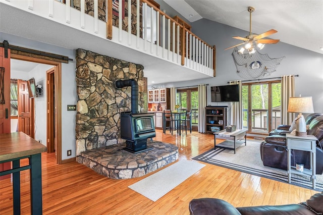 living area featuring baseboards, ceiling fan, high vaulted ceiling, hardwood / wood-style flooring, and a wood stove