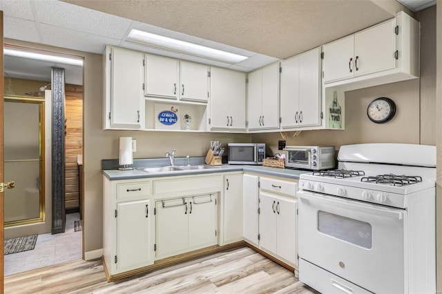 kitchen featuring a sink, stainless steel microwave, white range with gas cooktop, a toaster, and light wood-style flooring