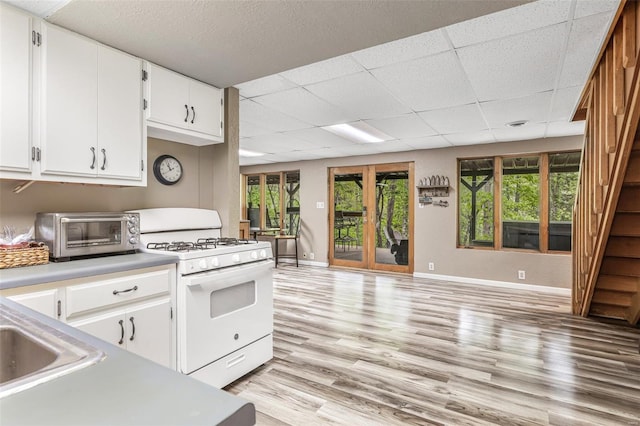kitchen featuring light countertops, a toaster, a paneled ceiling, light wood-type flooring, and gas range gas stove