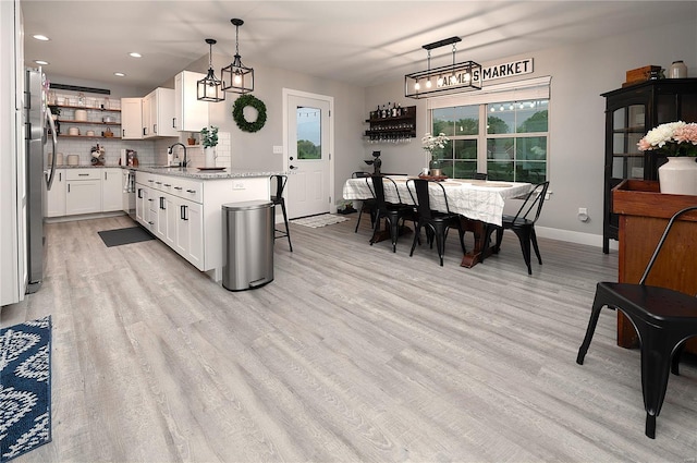 kitchen featuring open shelves, a sink, light wood-style flooring, baseboards, and decorative backsplash