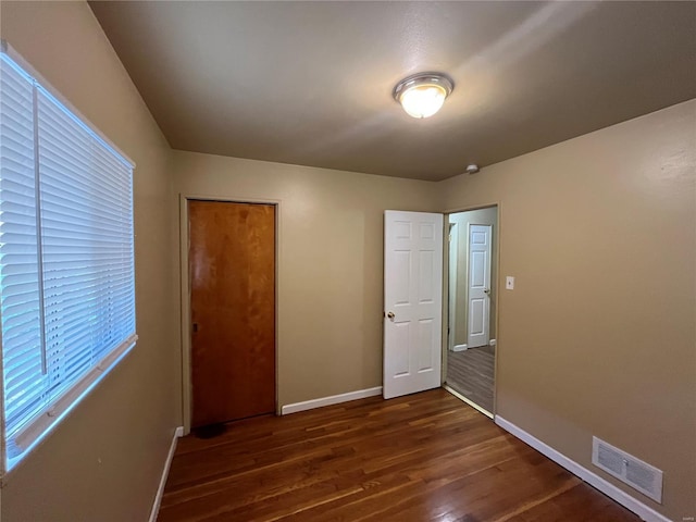 unfurnished bedroom with visible vents, baseboards, dark wood-style flooring, and a closet