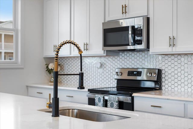 kitchen with appliances with stainless steel finishes, tasteful backsplash, light stone countertops, and white cabinets