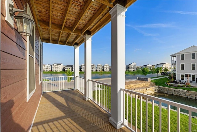 wooden terrace with a residential view, covered porch, a water view, and a lawn