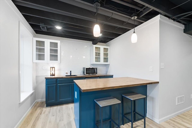 kitchen featuring visible vents, stainless steel microwave, wooden counters, and blue cabinetry