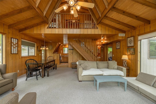 carpeted living area featuring ceiling fan, wooden walls, visible vents, and vaulted ceiling with beams