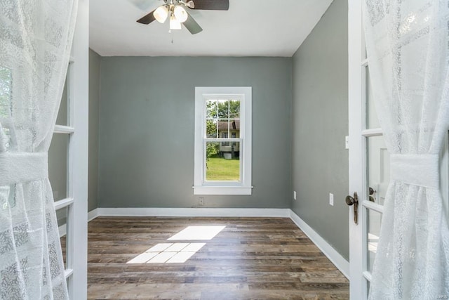 empty room with a ceiling fan, wood finished floors, french doors, and baseboards