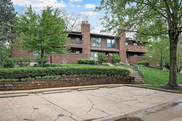 exterior space featuring a chimney, a yard, uncovered parking, and brick siding