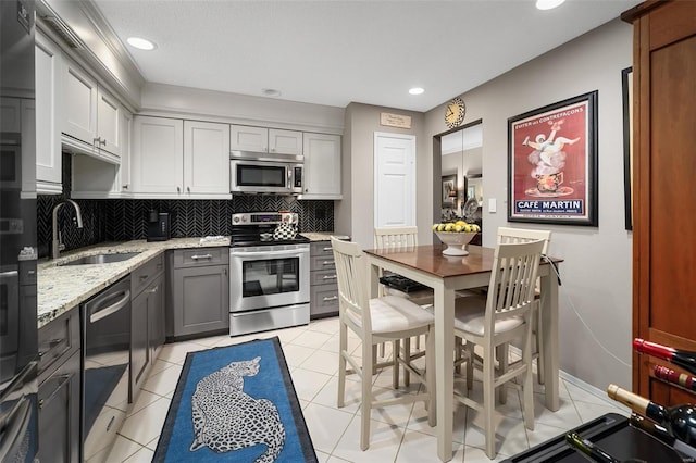 kitchen with backsplash, appliances with stainless steel finishes, a sink, gray cabinetry, and light stone counters