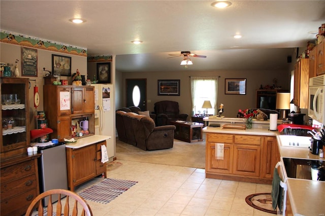 kitchen featuring brown cabinets, ceiling fan, light countertops, a peninsula, and white microwave