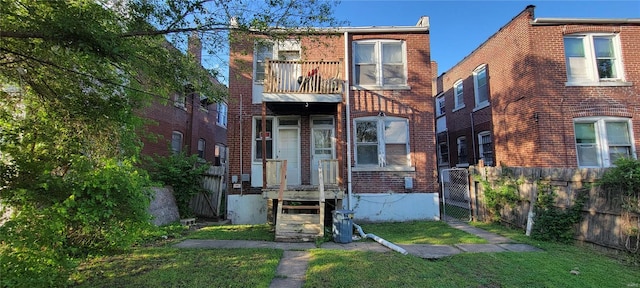 view of front facade featuring a front lawn, fence, a balcony, brick siding, and a gate