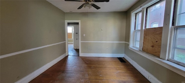 empty room featuring plenty of natural light, a ceiling fan, baseboards, and wood finished floors