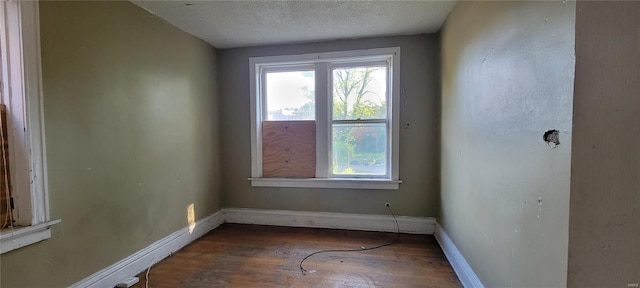 unfurnished room with a textured ceiling, baseboards, and wood finished floors