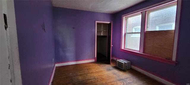 empty room with wood-type flooring, a textured ceiling, baseboards, and a wall mounted air conditioner