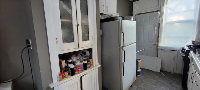 kitchen featuring glass insert cabinets, light countertops, freestanding refrigerator, and white cabinetry