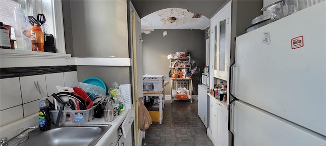 kitchen with a sink, freestanding refrigerator, and white cabinetry