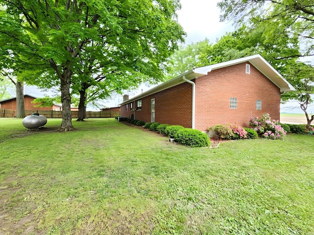 view of property exterior with brick siding, a lawn, and fence