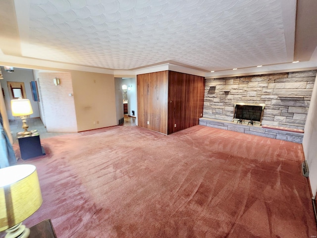 unfurnished living room featuring a raised ceiling, baseboards, a stone fireplace, and carpet