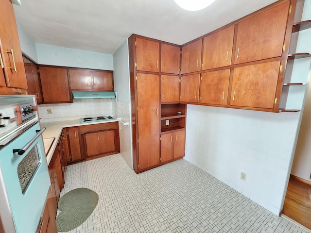 kitchen with under cabinet range hood, brown cabinets, white oven, and electric cooktop