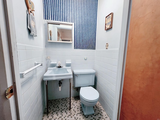 bathroom with a sink, a wainscoted wall, toilet, and tile walls