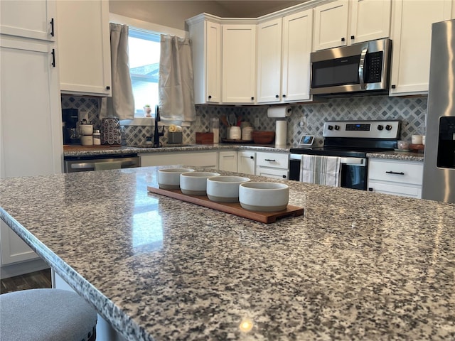kitchen featuring dark stone countertops, a sink, stainless steel appliances, white cabinetry, and backsplash
