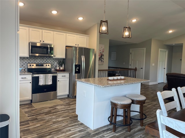 kitchen featuring a breakfast bar, stainless steel appliances, white cabinetry, dark wood-style flooring, and backsplash