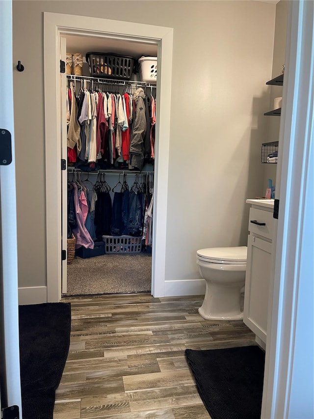 bathroom with toilet, wood finished floors, vanity, a spacious closet, and baseboards