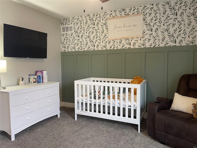 carpeted bedroom with a decorative wall, a wainscoted wall, visible vents, a crib, and wallpapered walls
