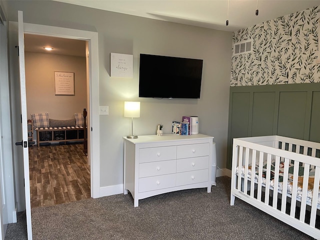 bedroom with wallpapered walls, a nursery area, visible vents, baseboards, and dark colored carpet