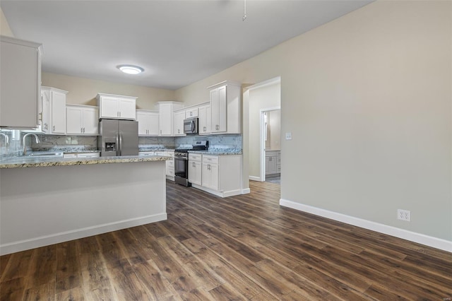 kitchen with a sink, a peninsula, tasteful backsplash, light stone counters, and appliances with stainless steel finishes