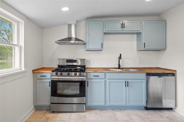 kitchen with wooden counters, baseboards, wall chimney exhaust hood, a sink, and stainless steel appliances