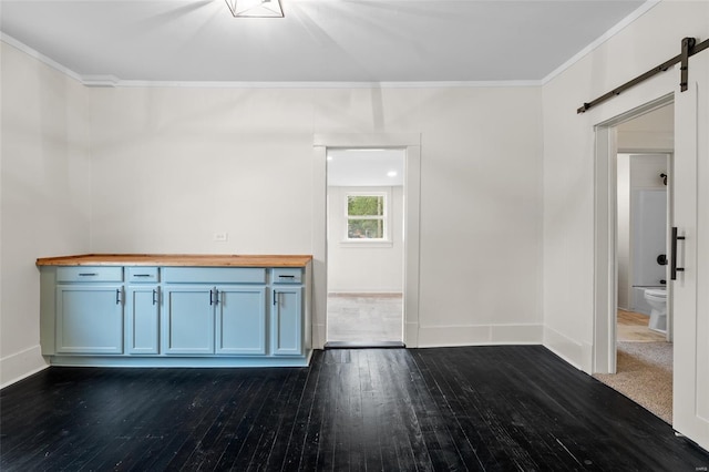 spare room with crown molding, a barn door, dark wood-style flooring, and baseboards