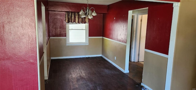 unfurnished dining area featuring baseboards, an inviting chandelier, and wood finished floors