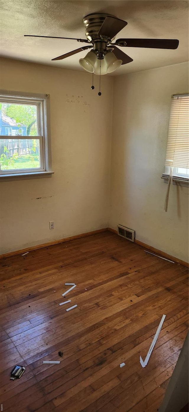 spare room with a ceiling fan, baseboards, visible vents, and dark wood finished floors