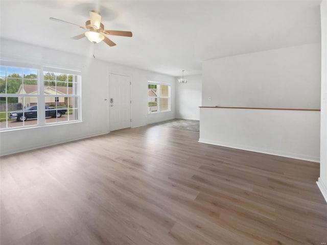unfurnished living room featuring a wealth of natural light, baseboards, wood finished floors, and ceiling fan with notable chandelier