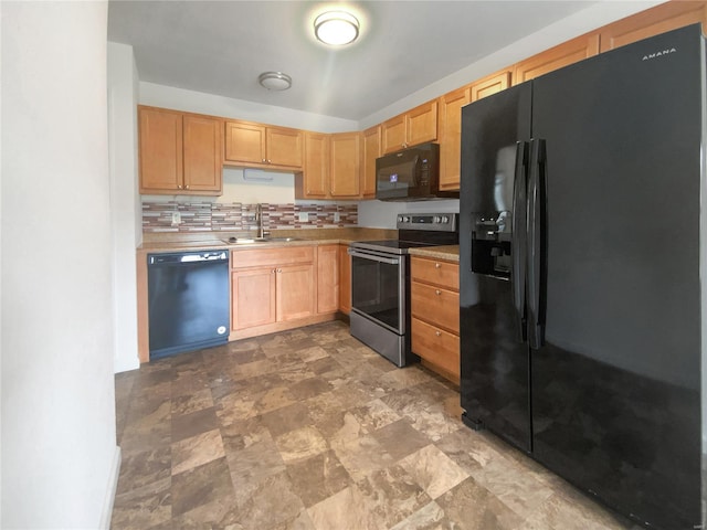 kitchen with a sink, stone finish floor, black appliances, light countertops, and tasteful backsplash