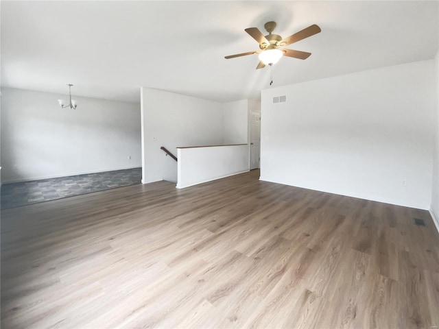 spare room featuring ceiling fan with notable chandelier, visible vents, and wood finished floors