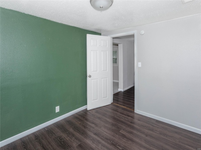 spare room with baseboards, dark wood-style floors, and a textured ceiling