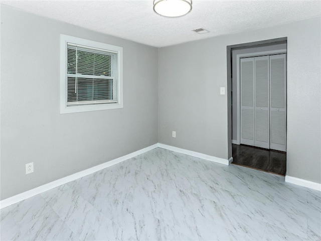 unfurnished room with marble finish floors, baseboards, and a textured ceiling