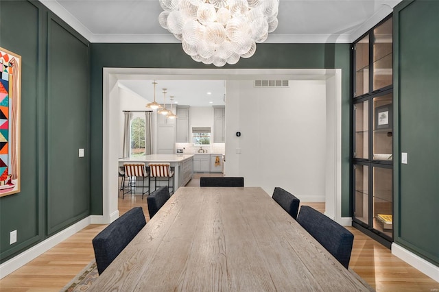 dining room featuring an inviting chandelier, ornamental molding, light wood-type flooring, and visible vents